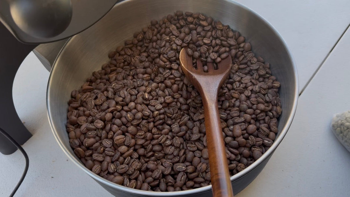 Coffee beans in a pot with a wooden spoon on a white surface